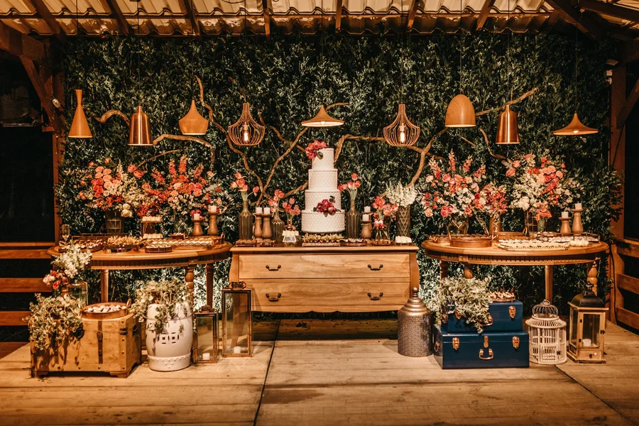 A dessert table under copper lamps banked with flowers